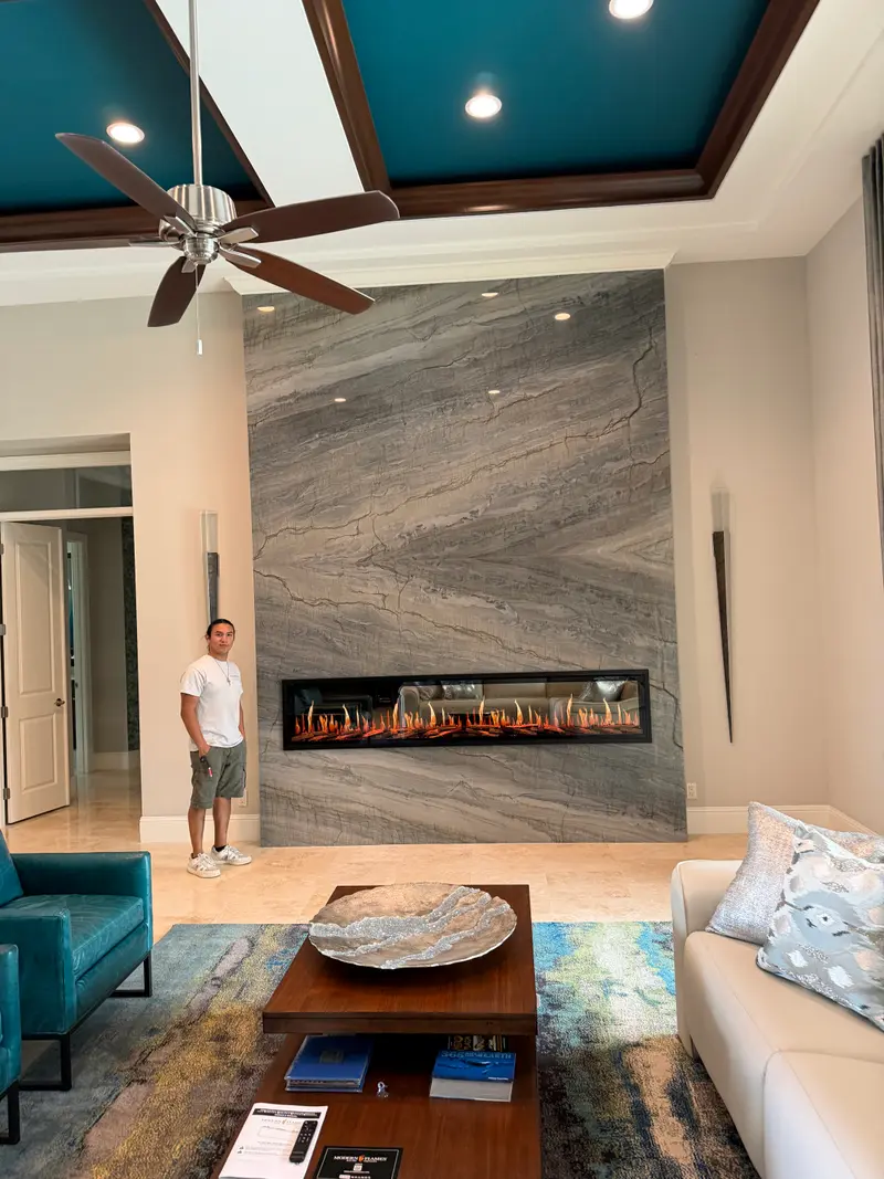 Floor-to-ceiling granite fireplace wall with a linear electric fireplace and a team member standing beside it for scale