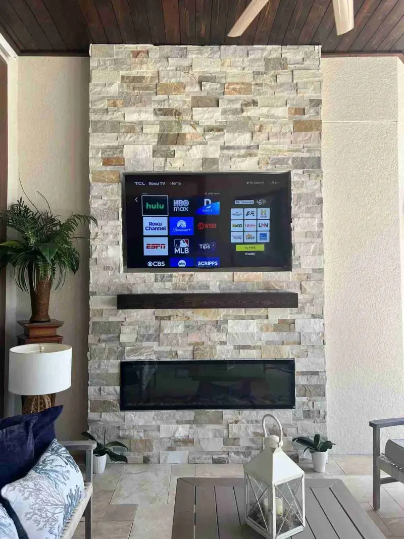 Ledgestone fireplace column with a TV above a linear electric fireplace on a covered lanai
