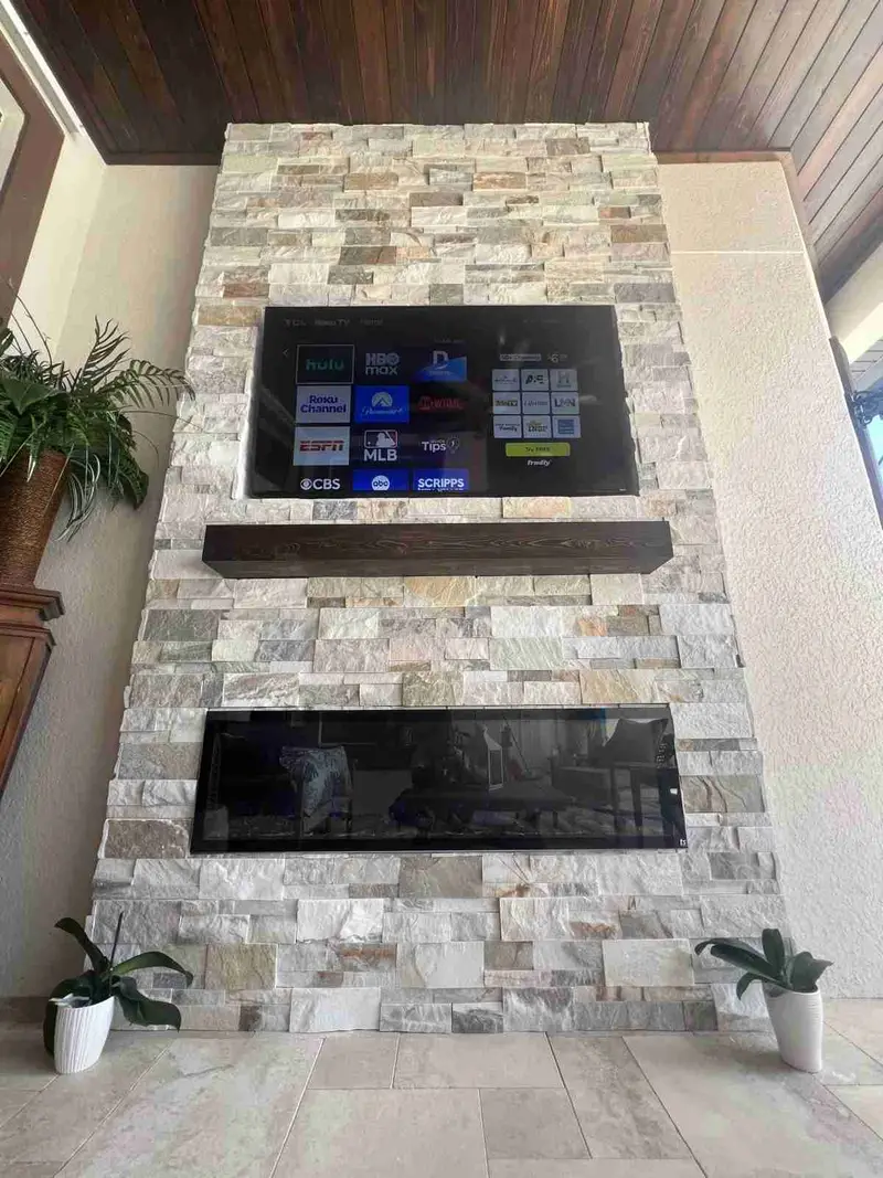 Full view of a ledgestone outdoor fireplace wall with a wood mantel on a covered lanai