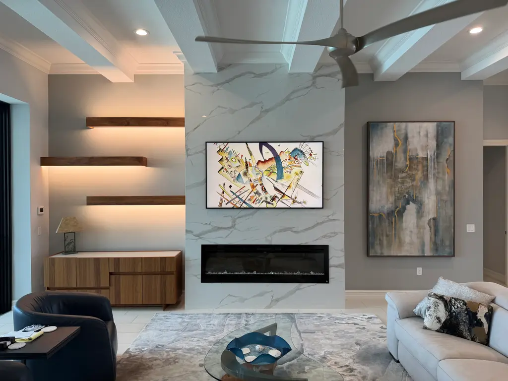 Marble-look feature wall with lit walnut floating shelves, an art-framed TV and a linear electric fireplace