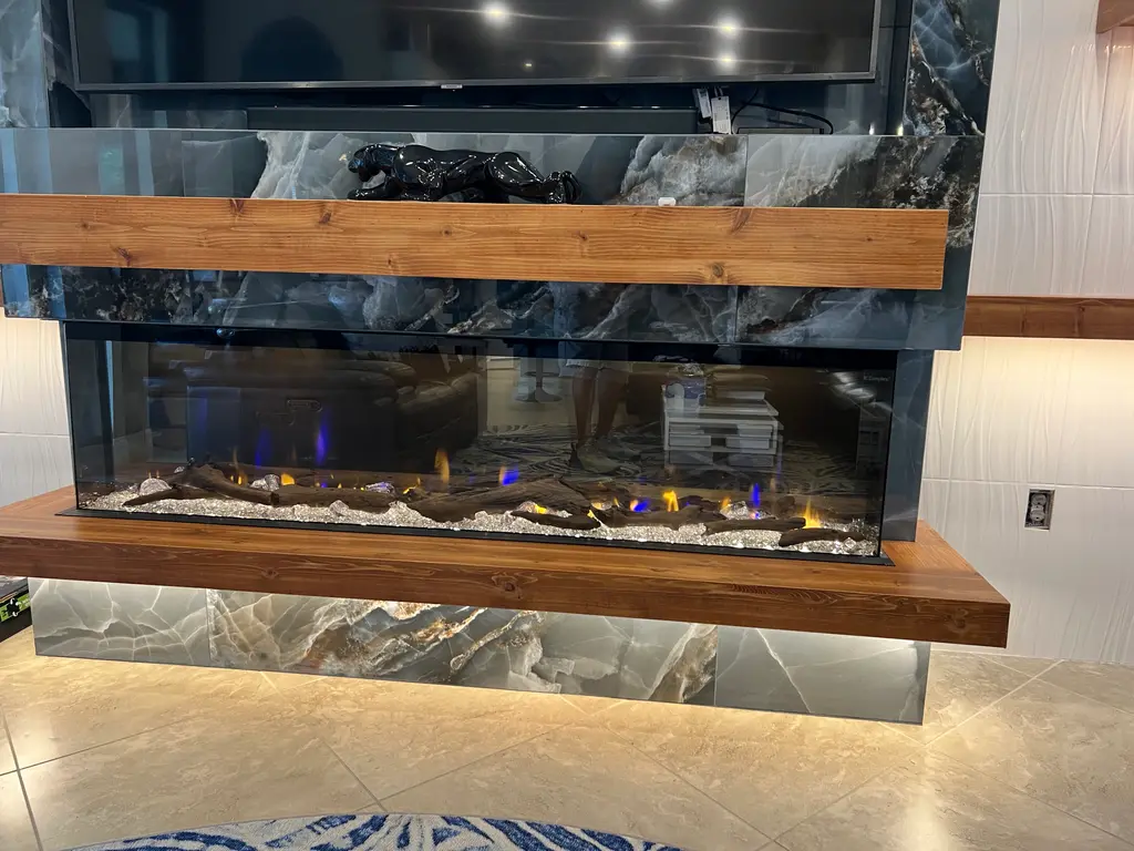 Close view of a wide electric fireplace set in blue onyx beneath a live-edge wood mantel