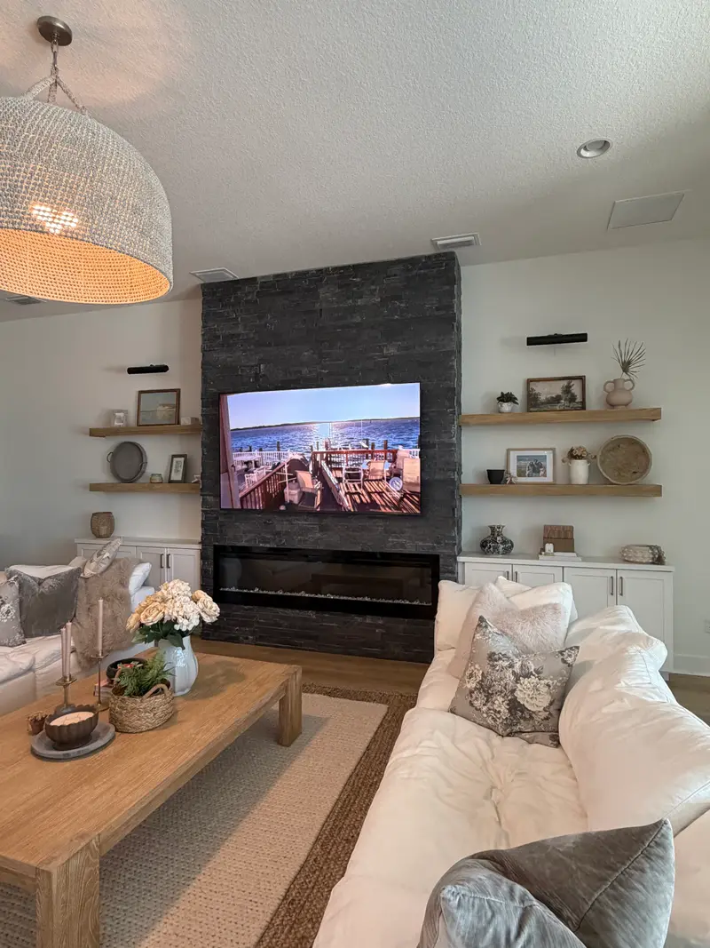 Dark stacked-stone fireplace wall with a linear electric fireplace flanked by floating shelves