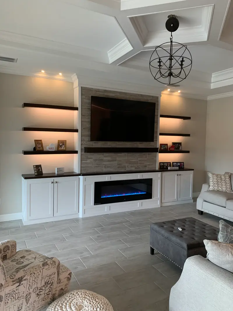 Stone media wall with dark floating shelves, white base cabinets and a linear electric fireplace