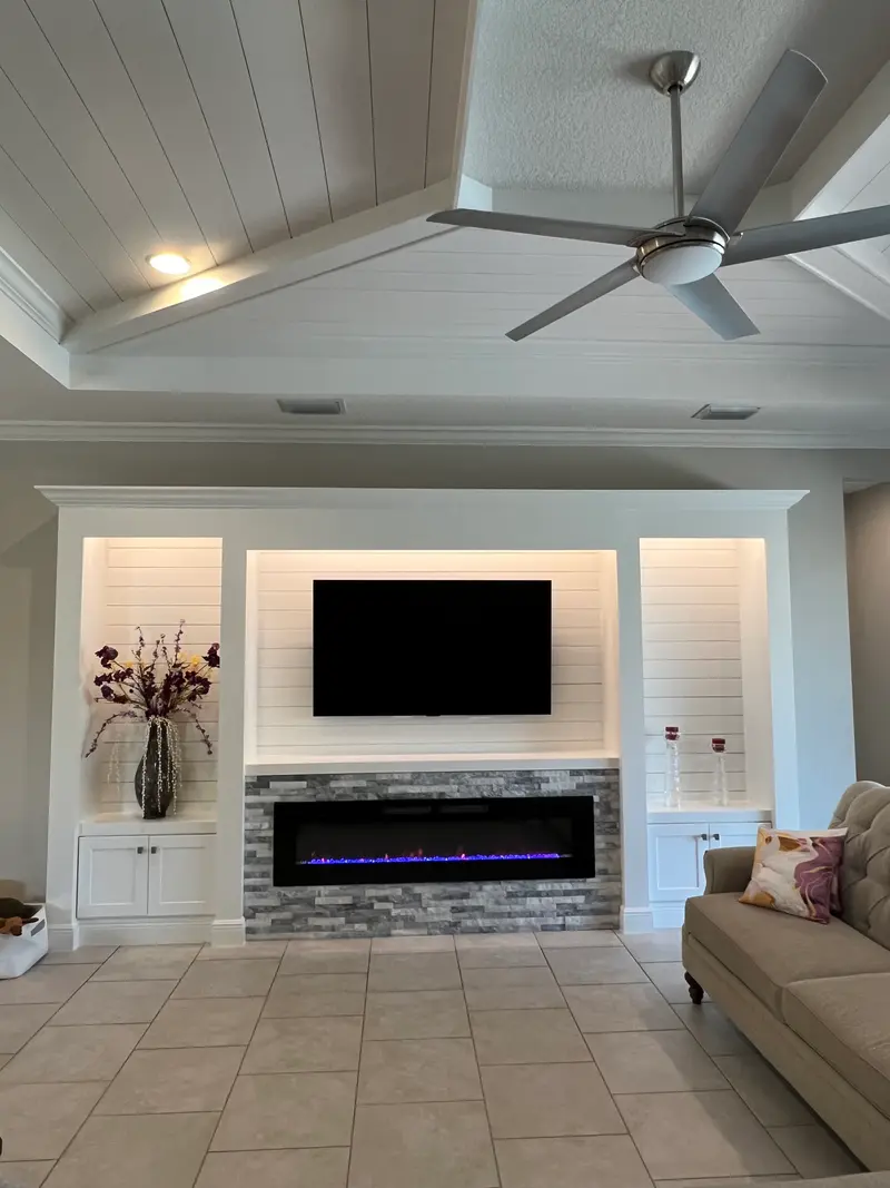 White shiplap built-in with lit side shelves and a stacked-stone surround around a linear fireplace