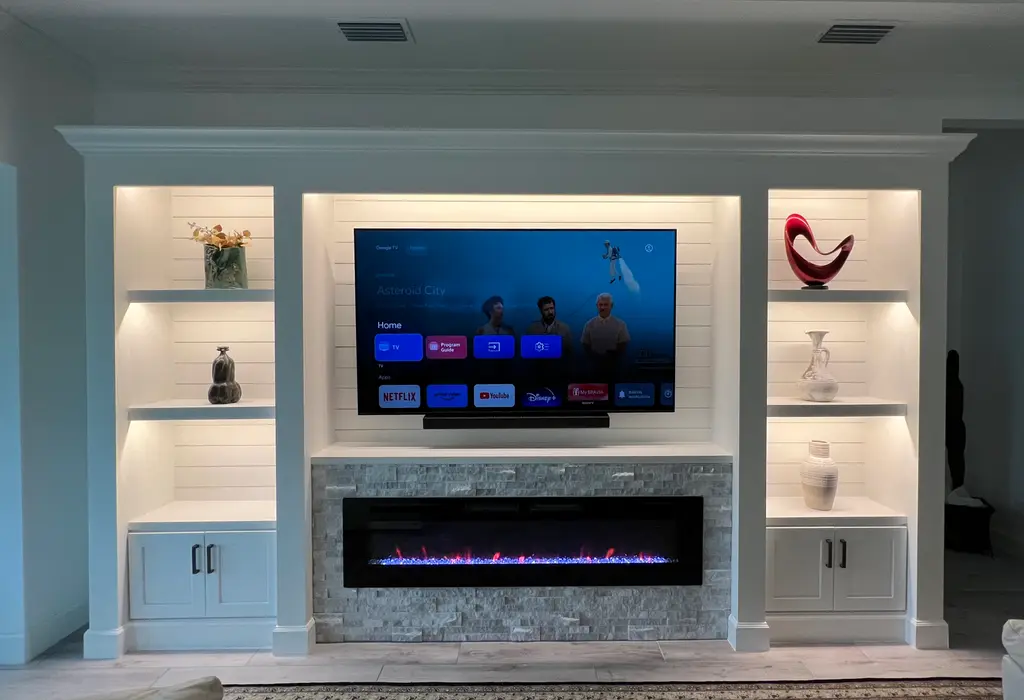 White built-in media wall with lit display shelves, cabinets and a stone-surround linear fireplace