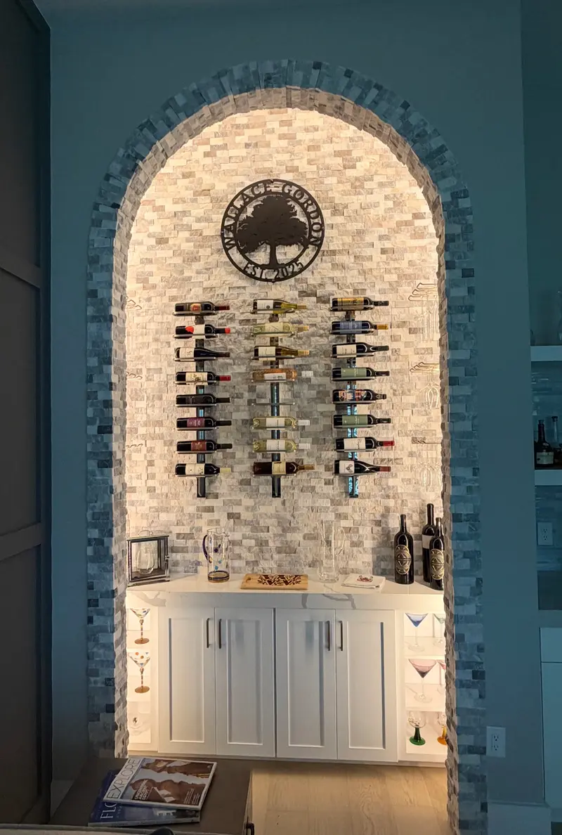 Front view of a lit stone-mosaic archway wine nook with bottle racks and cabinetry