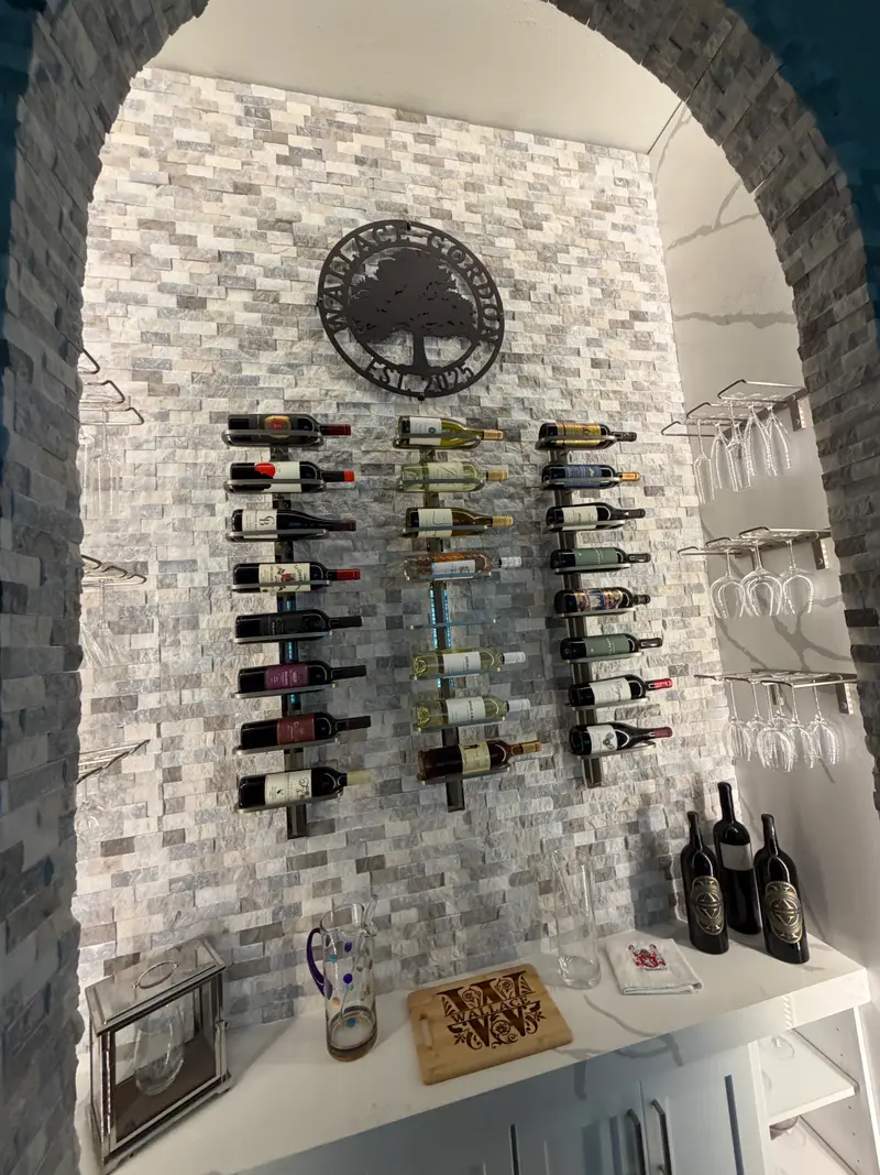 Stone mosaic wine wall with three columns of bottle racks and a white counter