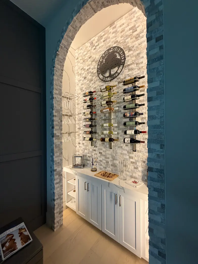 Side view of a stone-mosaic archway wine nook with glass holders and a white counter