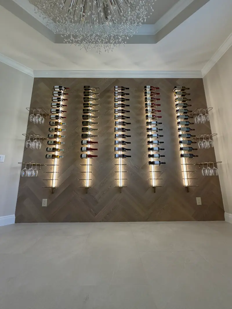 Herringbone wine wall with five backlit columns of floating bottles beneath a chandelier
